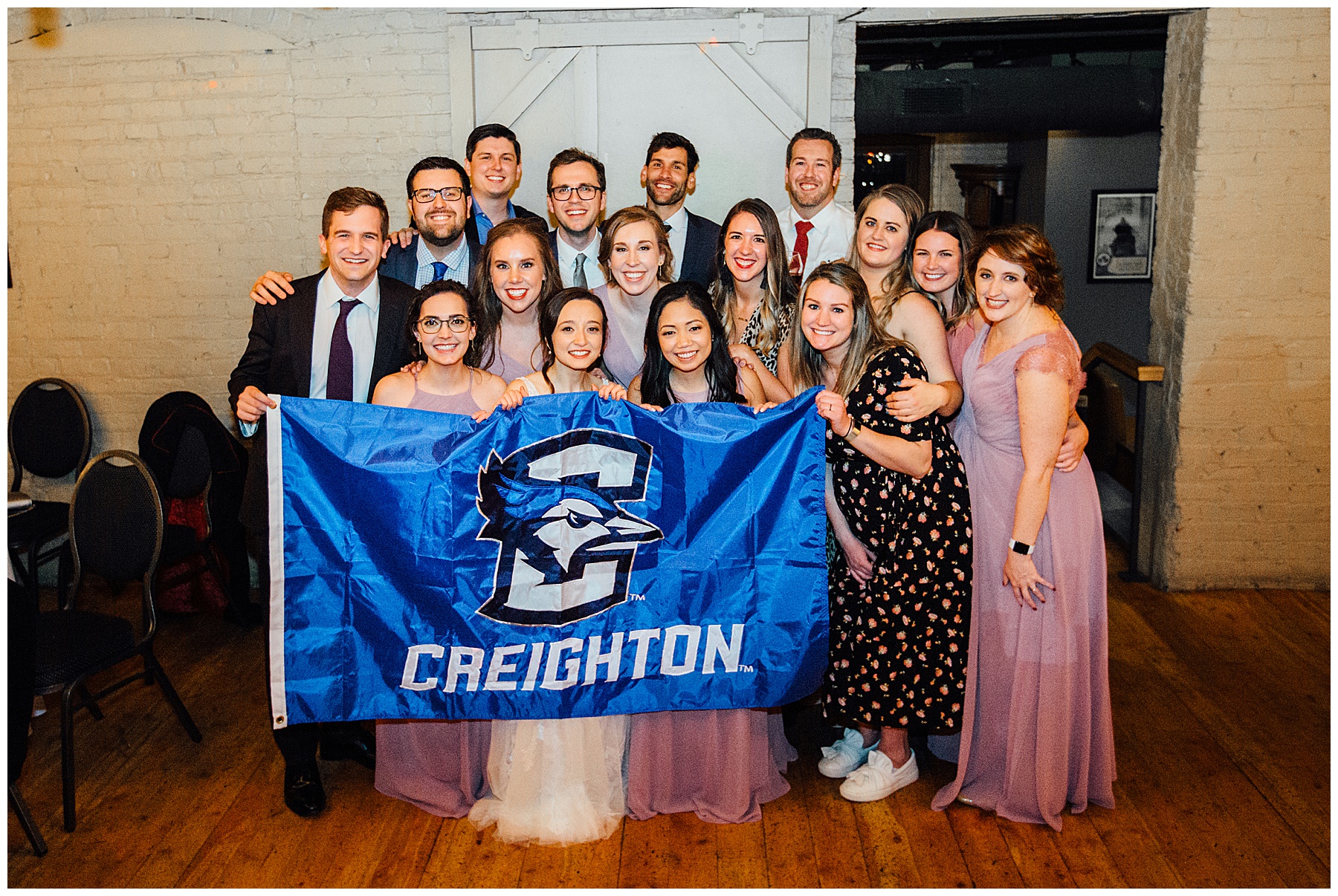Friends holding Creighton flag during at wedding reception
